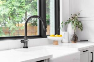Clean white quartz countertop next to a black faucet and open window